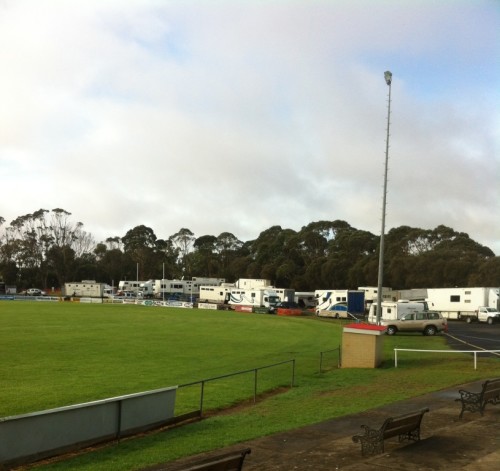 This picture shows all the truck parked on one side around the football oval.